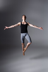 full length of elegant ballet dancer performing levitating with outstretched hands on dark grey