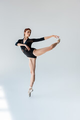 full length of flexible ballerina in black bodysuit stretching on grey