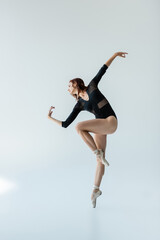 Fototapeta na wymiar full length of ballerina in black bodysuit and pointe shoes dancing on gray