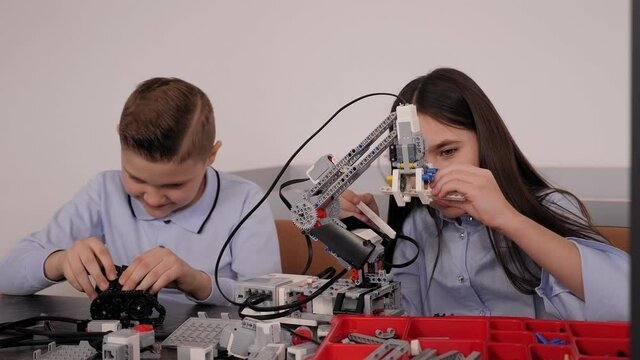 Children make a robot out of a robotic constructor at a desk with a computer at a robotics school.