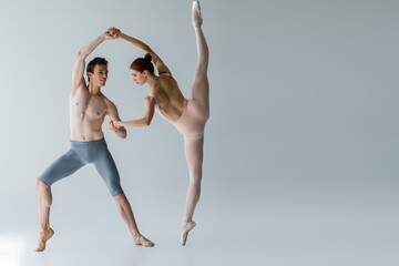 full length of young cheerful ballet dancer performing ballet dance with ballerina on grey - obrazy, fototapety, plakaty