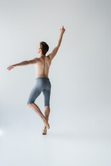 Fototapeta na wymiar young shirtless ballet dancer with raised hand on grey