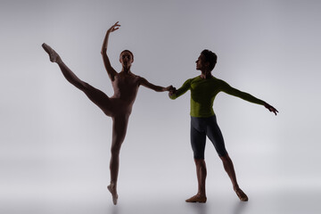 Fototapeta na wymiar silhouette of dancer holding hands with ballerina on grey
