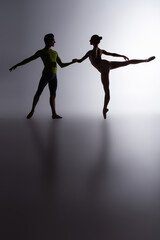side view of graceful ballerina in bodysuit dancing with partner on dark grey © LIGHTFIELD STUDIOS