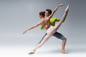 Fototapeta na wymiar full length of man and flexible woman performing ballet dance on grey