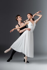 Fototapeta na wymiar full length of young graceful ballerina in white dress dancing with partner on dark grey