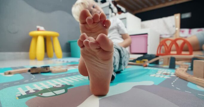 Closeup of cute child foot moving fingers laying on the floor in home barefoot. Carefree childhood enjoying in kid room after playing with toys