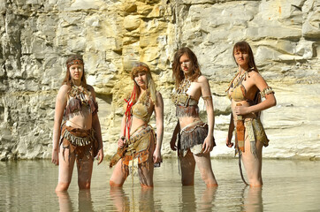 Four girls are dressed as Neanderthal warriors. They are 
covered with mud, filth and dirt and are...