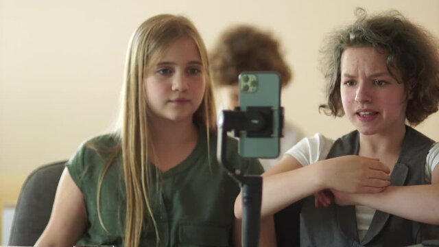 Two girls schoolgirls record a video at school. A girl with a stub and a smartphone in her hands. Electronic stabilizer and video blog concept