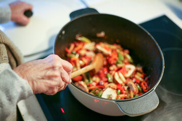Fototapeta Kobieta gotująca i mieszająca jedzenie w brytfannie obraz