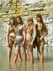 Four girls are dressed as Neanderthal warriors. They are 
covered with mud, filth and dirt and are...