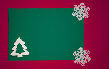 Minimalistyczne tło na kartkę z życzeniami świątecznymi w czerwonym i zielonym kolorze z białą choinką i płatkami śniegu.