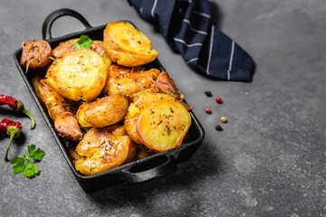 Crispy salt and vinegar smashed roast potatoes in cast iron skillet on dark background. Top view, copy space.