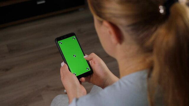 Close-up of woman's hand browsing smartphone with green screen at home. Woman at home relaxing reading on the smartphone with pre-keyed green screen.