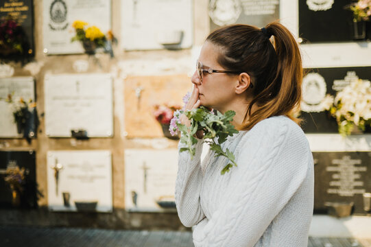 Mourning woman standing near columbarium wall and touching mouth