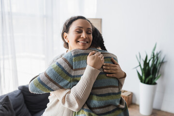 joyful african american woman with closed eyes hugging teenage daughter at home