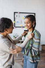 african american woman touching pigtails of happy teenage daughter