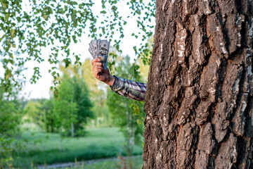 a hand sticks out from behind a tree and offers money. quick money