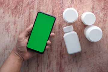 many pill container and hand hold a smart phone on wooden table 