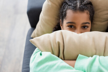 top view of depressed african american girl obscuring face with pillow while lying at home