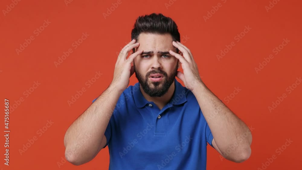 Wall mural Sad upset worried disturb displeased young bearded brunet man 20s years old wears blue t-shirt sigh suspire sithe put hands on face say what why isolated on plain red orange background studio portrait