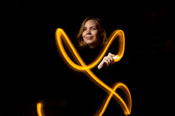 Write with light at long exposure in the dark. A middle-aged woman paints with a flashlight.