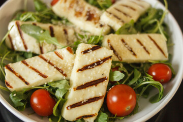 Traditional greek fried halloumi cheese on a white plate with herbs and cherry tomatoes. View from above.