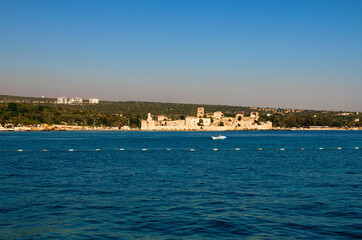 Wide angle landscape view of blue water of Mediterranean Sea and city beach with ancient ruins of Romanian castle. Blue sky background. Famous touristic place