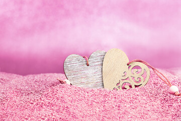 Two wooden hearts on pink sand against blurred background with bokeh. Valentine's Day. Copy space