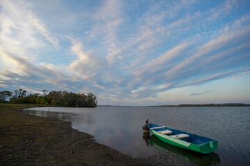 The boat is moored off the coast. There are small ripples on the water. There are beautiful clouds in the sky.