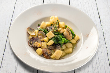 Potato dumplings gnocchi with clams and turnip greens in white plate on white wooden table