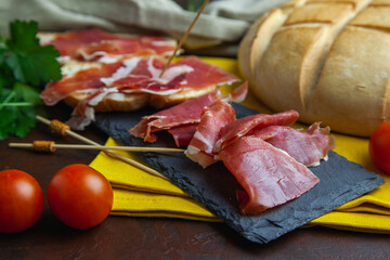 Lonchas de jamón serrano ibérico sobre un plato de piedra con algunos tomates y pan