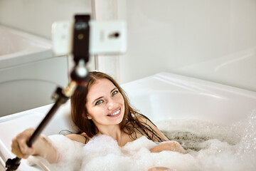 Whirlpool bath in hotel room, woman communicates online by fixing her phone on selfie stick.