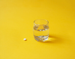 glass of water and a pill on a yellow background