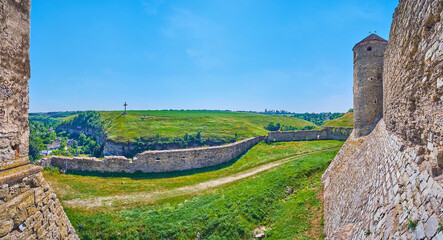 Panorama with ruins of outer wall of Kamianets-Podilskyi Castle and the green meadow in background,...