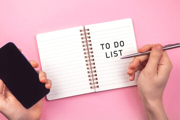 Obraz premium Empty to do list for new year. Notebook on pink table, planning concept background. Hand with smartphone and pen. Top view photo