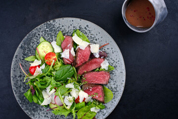 Modern style traditional fried dry aged bison beef rump steak slices with vegetable, lettuce and mustard raspberry dressing served as top view on a Nordic design plate