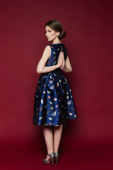 Young woman in printed blue dress holding hands behind her back in yoga gesture, relaxing meditating, trying to calm down, posing on a red background