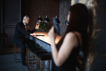 Man and woman, stills from the film. Bald man sits in a bar with a glass of wine and a gun,...