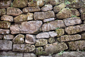 A texture made of big grey stones covered with moss and grass.