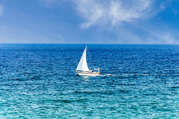 Scene of a small boat with sail in the middle of the blue ocean