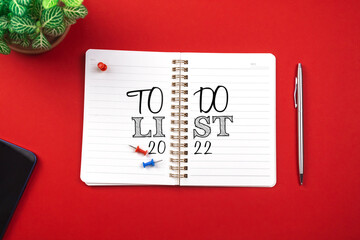 Planning for new year 2022 concept. Notebook with to do list. Red background, silver pen, copy space and top view photo