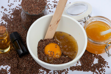 Brown flax seeds, linseeds oil, egg and honey on white background. Home made cosmetics ingredients.