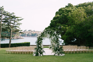 Fototapeta na wymiar Wedding arches surrounded by rows of chairs on a green lawn near the sea