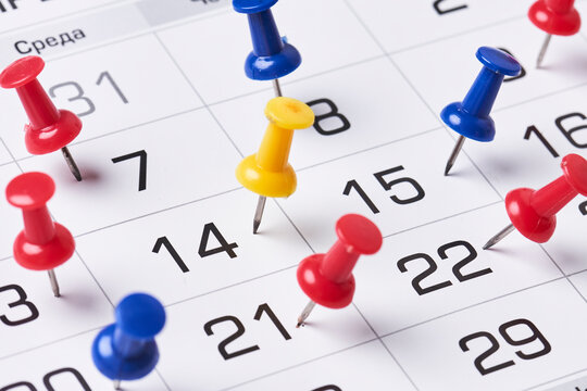 Colored push pins on monthly calendar page. Calendar appointments. Multicolored push pins on calendar. Marked event day, business appointment, meeting with pin. Close-up of push pins on calendar date