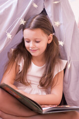 Little girl is sitting in a hovel and reading an interesting book