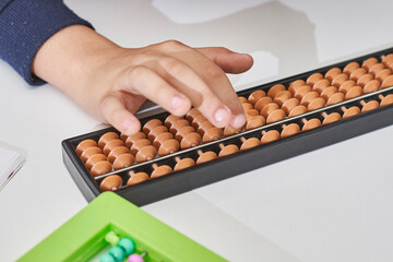 Doing mental math or mental arithmetic. Hand of little boy using abacus for calculating. Learning to use abacus on mental math courses. A kid doing math at home with abacus