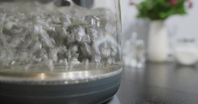 Close-up of boiling water in transparent glass container. Seething clear liquid