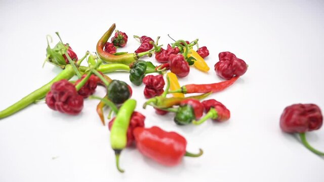 Bunch of colourful hot peppers dropping into a wooden cutting board