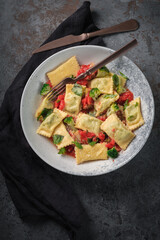 Italian square ravioli with spinach, tomato sauce and broccoli in a plate on a black stone background. Dish pasta ravioli
